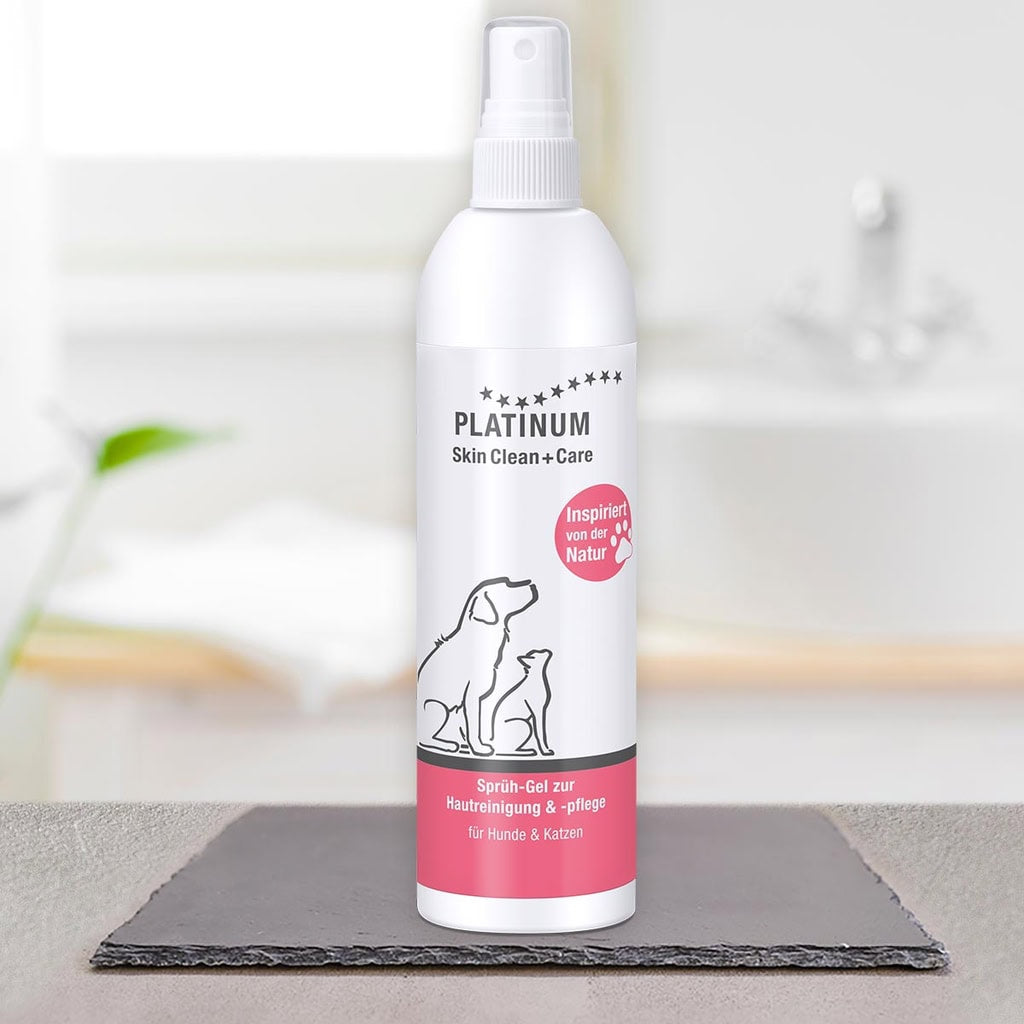 Steklenička PLATINUM Skin Clean + Care, Nega Kože za Pse in Mačke, stoji na črni površini z zamegljenim ozadjem kopalnice. Na etiketi so prikazane ilustracije psov in mačk ter poudarjena naravna nega kože za srbeča koža.