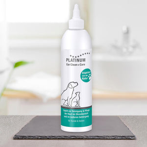 Bela steklenička PLATINUM Ear Clean + Care, Nega Ušes za Pse in Mačke, stoji na temni preprogi. Na etiketi sta črtni risbi psa in mačke z zelenimi poudarki, idealno za nego pasjih in mačjih ušes.